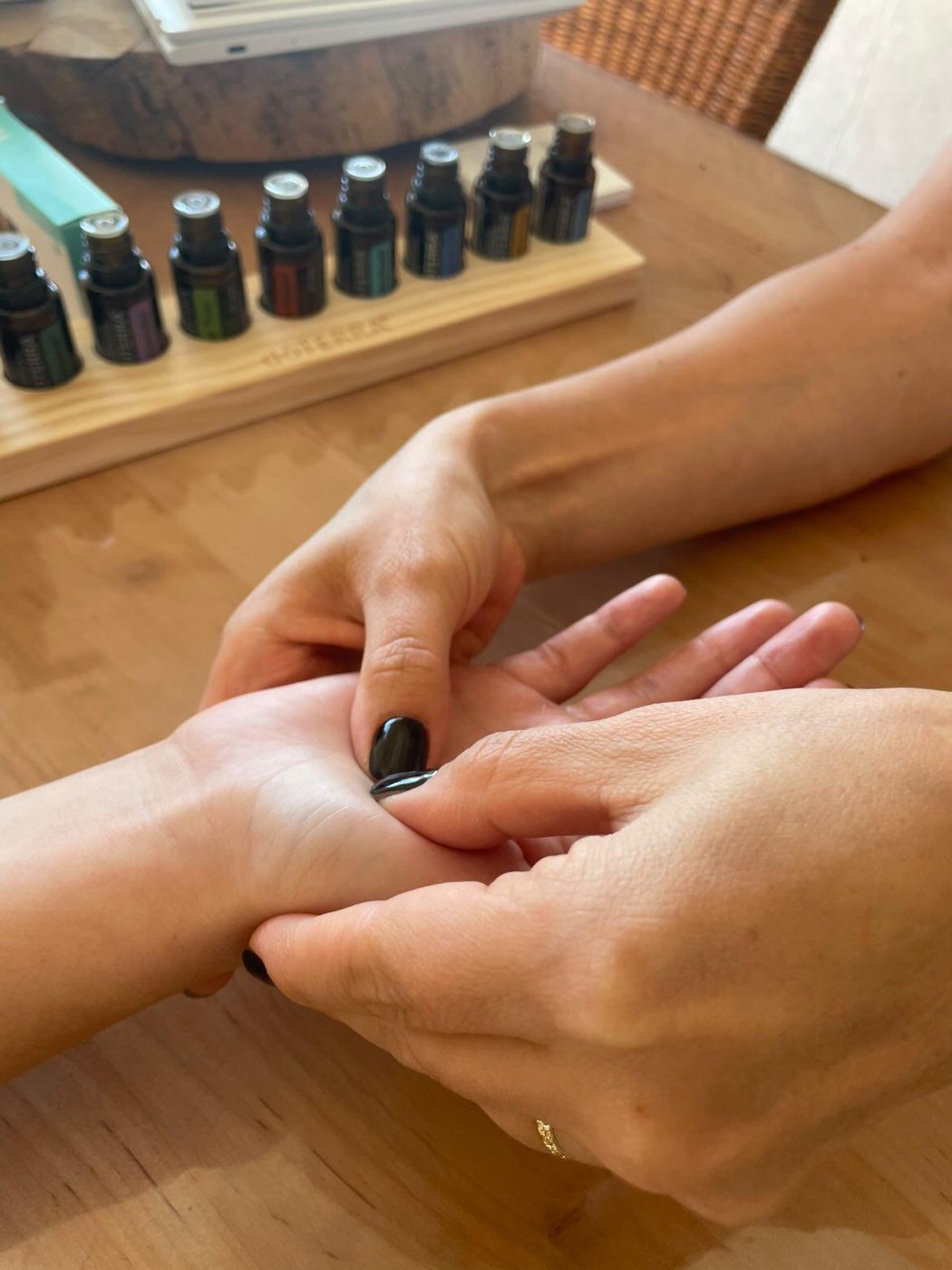 Des mains pratiquant le soin AromaTouch sur une paume, devant une rangée d'huiles essentielles